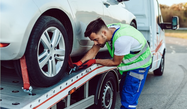 Technician performing emergency roadside assistance and towing services kneeling down to secure wheels using the MobiWork emergency roadside assistance and towing services software solution